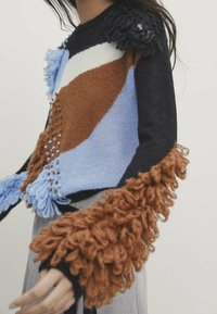 Bunt gestrickter Pullover mit braunen, blauen und schwarzen Abschnitten. Strukturiert fransige Ärmel und Garntöne verleihen Details.