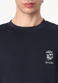 T-shirt en coton bleu marine avec un col rond côtelé ; présente un design brodé blanc d'une scène de café sur la poitrine.