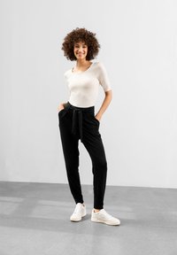 Svarta högmidjade byxor med knytning i midjan, tillsammans med en åtsittande krämfärgad skjorta och vita sneakers. Slätt tyg, avslappnad siluett.