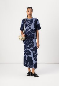 Set tricotat cu un design floral în nuanțe de bleu marin pe un fundal bleu deschis. Întregul outfit include un top cu mânecă scurtă și o fustă lungă, asortat cu o geantă crem.