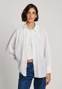 Weißes Baumwollhemd mit klassischem Kragen, entspannter Passform und langen Ärmeln, kombiniert mit hoch taillierten blauen Jeans.