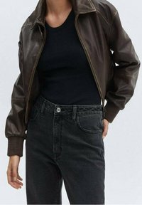 Chaqueta bomber de cuero marrón con cuello y puños acanalados, combinada con jeans de tiro alto gris oscuro. Costuras mínimas y bolsillos clásicos.