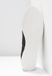 Chaussure en cuir noir avec coutures décoratives, semelle en caoutchouc blanche texturée et indication de taille 37, inclinée sur un fond neutre.