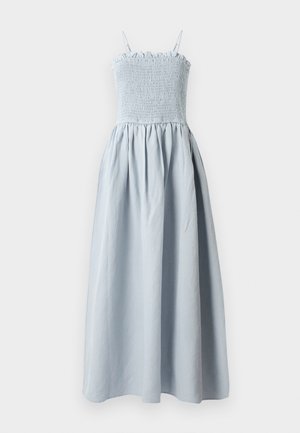 Lyseblå, lang bomullskjole med smock-bodice, tynne skulderstropper og en flytende, samlet skjørt. Har en volangkant øverst.