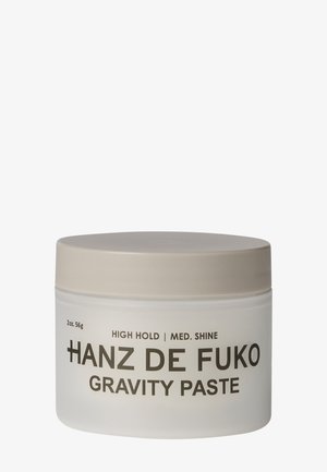 Lille hvid krukke med beige låg mærket Hanz de Fuko Gravity Paste, høj hold, medium glans, 2 ounce.