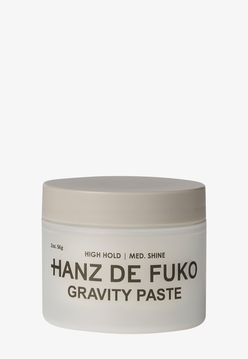 Petit pot blanc avec couvercle beige étiqueté Hanz de Fuko Gravity Paste, tenue élevée, brillance moyenne, 2 onces.