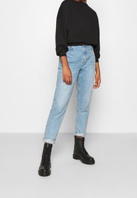 Jean taille haute bleu clair, ourlets retroussés, associé à des bottes de combat noires à lacets. Haut noir oversize à manches longues. Look simple et décontracté.