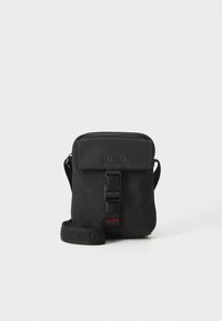 Borsa a tracolla nera realizzata in tessuto resistente. Presenta una chiusura con pattina, una tracolla regolabile con logo impresso e un dettaglio con fibbia anteriore.