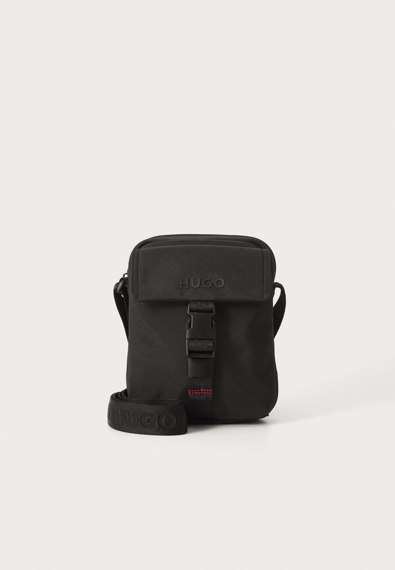 Borsa a tracolla nera realizzata in tessuto resistente. Presenta una chiusura con pattina, una tracolla regolabile con logo impresso e un dettaglio con fibbia anteriore.