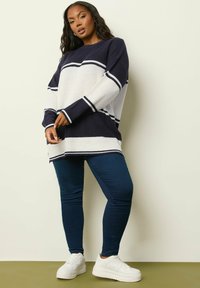 Marinblå och vit randig översize stickad tröja med långa ärmar, kombinerad med mörkblå leggings och vita sneakers. Avslappnad passform med sidslitsar.