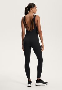 Fekete ujjatlan body, V-háttal és több átlós pánttal. Simás anyagból készült, fitted lábakkal és sportos kivitelben.