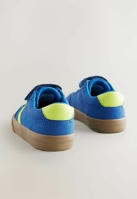 Blauwe suède schoenen met een gladde groene accent en klittenbandsluiting. Heeft een tan rubberen zool en afgeronde hak voor extra comfort.