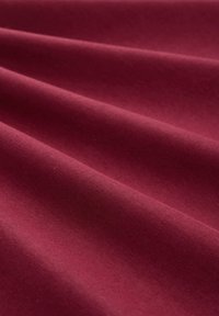 Weiches, glattes bordeauxrotes Gewebe mit sanften Falten, die diagonale Schatten und Lichtreflexe über die Oberfläche erzeugen.