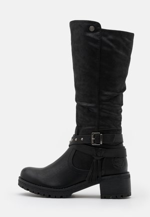 Botte noire mi-mollet avec un talon carré, une boucle décorative et une sangle, une semelle texturée, et un petit bouton rond en métal près du haut.