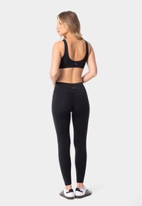 Sostén deportivo negro y leggings de cintura alta hechos de tela elástica. Presenta un diseño de espalda de nadador y un branding mínimo. Combinado con zapatos en blanco y negro.