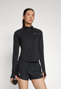 Crna majica s dugim rukavima i crne kratke hlače od laganog materijala, s diskretnim Nike logom na svakom komadu. Uključena boca za vodu.