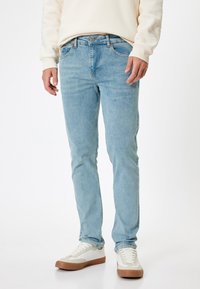 Ljusblå denimjeans med smal passform, femfickorsdesign, kontrasterande sömmar och detaljer i koppar. Bärs med vita sneakers.