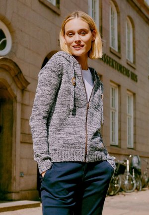 Sivá pletená mikina na zips s textúrovaným vzorom, s kapucňou na šnúrku a detailmi z dreva, kombinovaná s tmavými nohavicami.