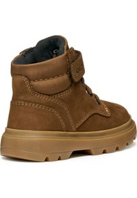 Botín de ante marrón con un cuello acolchado, una correa de Velcro, costuras en contraste y una suela de goma con patrones de agarre texturizados.