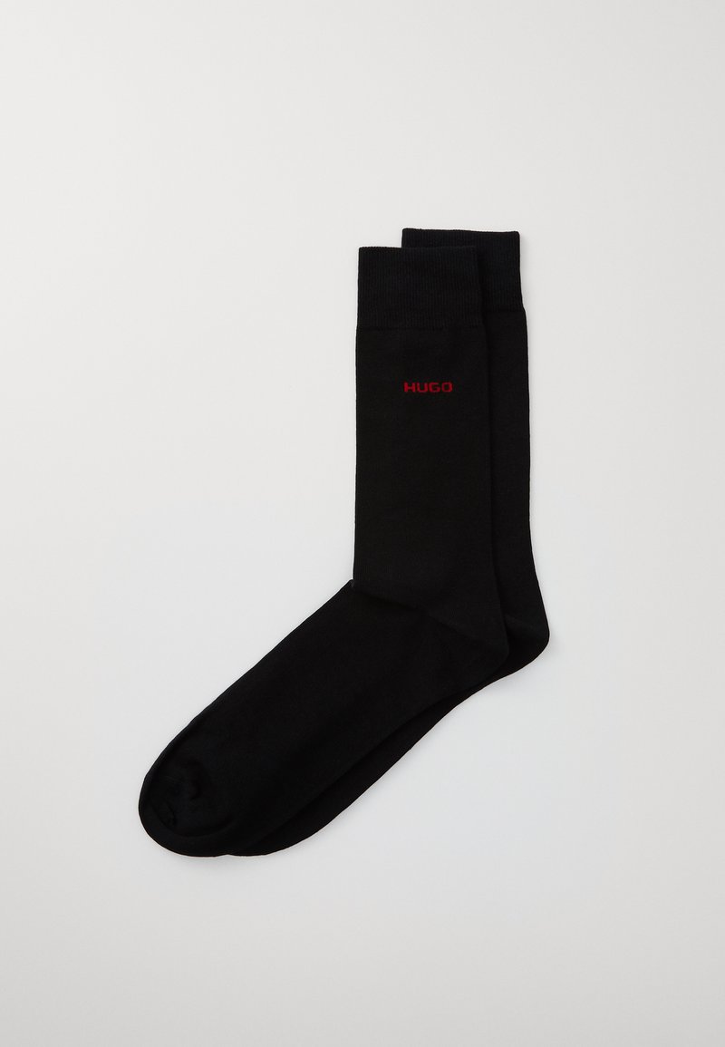 Chaussettes noires en coton avec une texture lisse et un haut côtelé. Le logo de la marque "HUGO" est affiché en rouge.