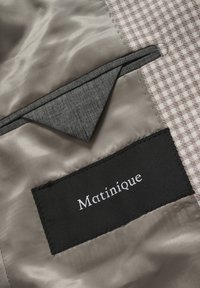 Beige-braun karierte Jackenfütterung mit grauer Taschenklappe und einem schwarzen Matinique Markenlabel, das innen eingenäht ist.