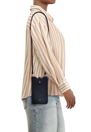 Persona con camiseta de rayas beige y blanca y jeans claros, llevando un pequeño bolso bandolera negro con correa sobre el hombro.