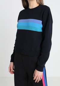 Suéter negro de punto con cuello redondo y mangas largas, que presenta rayas horizontales de azul y turquesa a lo largo del pecho.