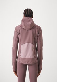 Casaco desportivo lilás claro com capuz, tecido texturizado, detalhes em painéis e um bolso com fecho de correr na parte inferior das costas.