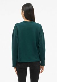 Sudadera de color verde con hombros caídos, mangas largas y escote redondeado; presenta una textura suave y un corte relajado.