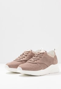 Sneakers z jasnobrązową cholewką z zamszu z perforowanymi detalami, kremowymi akcentami i grubą białą podeszwą o teksturowanym wykończeniu.