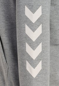 Grauer Hoodie aus strukturiertem Stoff mit einem vertikalen weißen Zickzackmuster entlang des linken Ärmels.