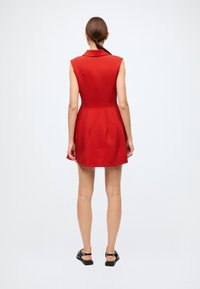 Red sleeveless dress with a collar, fitted bodice, and pleated skirt, made from smooth fabric. Black sandals with strap details.