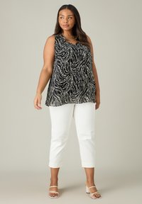 Svart ärmlös topp med vit virvlande mönster, har en volangkrage; matchas med vita cropped byxor och nude sandaler med remmar.