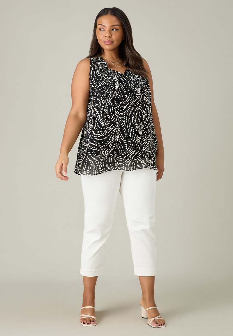 Svart ärmlös topp med vit virvlande mönster, har en volangkrage; matchas med vita cropped byxor och nude sandaler med remmar.
