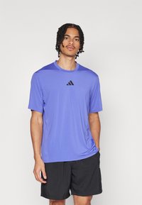 Purple athletic t-shirt made of lightweight fabric, featuring short sleeves, round neck, and black logo on the chest. Worn with black shorts.