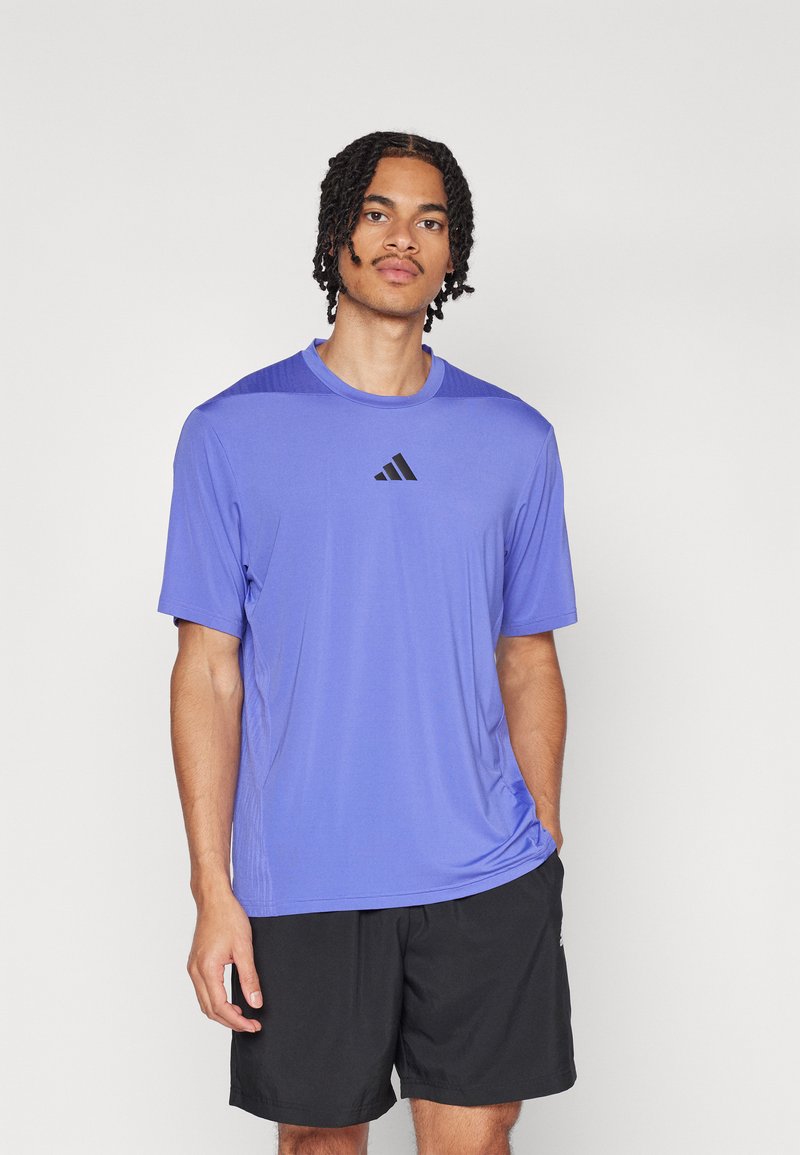 Purple athletic t-shirt made of lightweight fabric, featuring short sleeves, round neck, and black logo on the chest. Worn with black shorts.