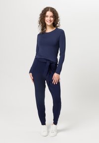 Haut à manches longues bleu marine avec un col rond, associé à un pantalon bleu marine fuselé doté d'une ceinture à nouer et de poches latérales, complété par des baskets blanches.