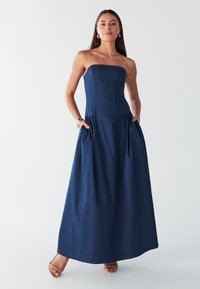 Tmavomodré maxi šaty bez ramienok s priliehavým živôtikom, plisovanou sukňou a vreckami. Vyrobené z hladkej látky, s čistým dizajnom.