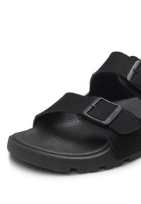 Czarna sandałka z odkrytymi palcami, z fakturowaną wkładką i dwoma regulowanymi zamszowymi paskami z metalowymi klamrami, z których jeden jest z wytłoczonym logo "BOSS".