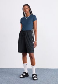 Kortärmad mörkblå t-shirt ihop med svarta meshshorts med dragsko. Svarta sandaler med vita detaljer och knälånga vita strumpor.