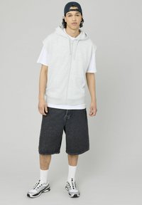 Haut sans manches gris avec fermeture éclair à l'avant, associé à un t-shirt blanc, un short en denim noir, des chaussettes blanches et des baskets noir et blanc.