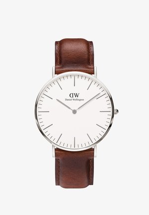 Braunes Lederarmbanduhr mit einem Gehäuse aus silbernem Edelstahl. Das weiße Ziffernblatt zeigt minimalistische Stundenmarkierungen und das "DW"-Logo, das oben in der Mitte positioniert ist.