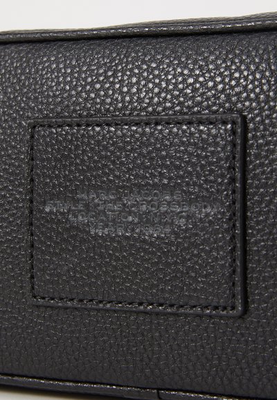 Sort læder crossbody taske med en struktureret overflade, prægning med brandinglabel og detalje med topstikning. Kompakt rektangulær form.