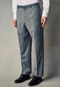 Pantalones grises ajustados con una tela texturizada, pernera recta y parte delantera plana, combinados con zapatos negros de cordones.