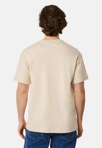 Beige cotton t-shirt with a classic crew neck and short sleeves, displayed from the back, featuring a relaxed fit and smooth texture.