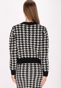 Černobílý pletený svetr s motivem houndstooth, ribbovaným límcem a manžetami, s cropped designem a texturovanou tkaninou.