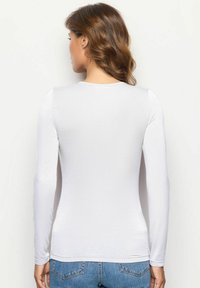 Camicia bianca a maniche lunghe realizzata in un tessuto liscio e aderente, con scollatura rotonda e orlo dritto, abbinata a jeans blu.
