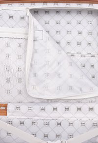 White interior of a suitcase featuring a geometric pattern. Includes a mesh zip pocket and a fabric divider with logo accents.