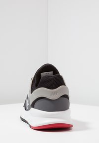 Černošedá teniska s síťovaným svrškem, polstrovaným límcem a výrazným šedým logem na patě. Má bílou mezipodešev a červenou podrážku.