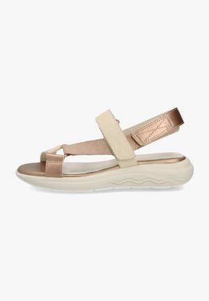 Sandales beige et or rose avec une tige synthétique, des brides ajustables, une semelle intérieure rembourrée et une semelle extérieure en caoutchouc blanc à motif ondulé.